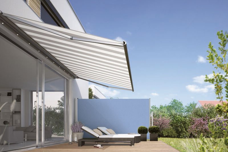 A stylish terrace with a retractable awning and loungers, surrounded by greenery and a blue wall. A stylish terrace with a retractable awning and loungers, surrounded by greenery and a blue wall.