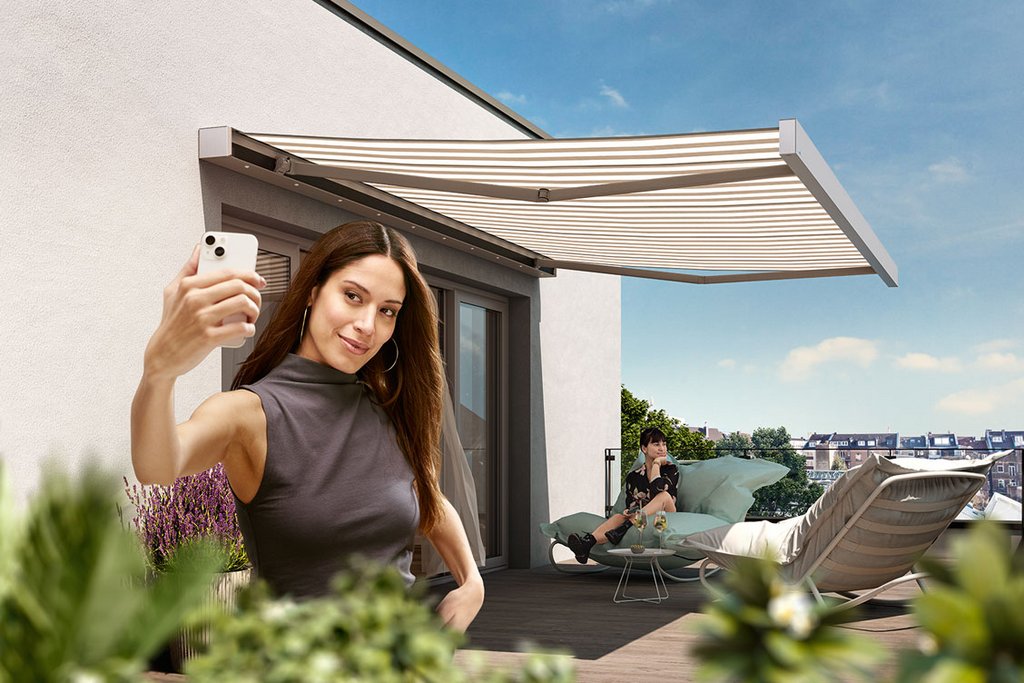 A woman taking a selfie on a balcony with a retractable awning and green plants nearby. A woman taking a selfie on a balcony with a retractable awning and green plants nearby.