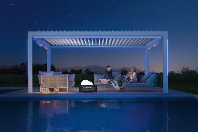A stylish outdoor seating area under a modern structure, illuminated, beside a calm pool at night. A stylish outdoor seating area under a modern structure, illuminated, beside a calm pool at night.