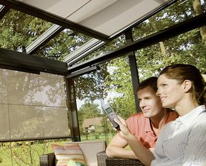 A couple enjoying time together in a modern winter garden with glass walls and a remote control for shading.
