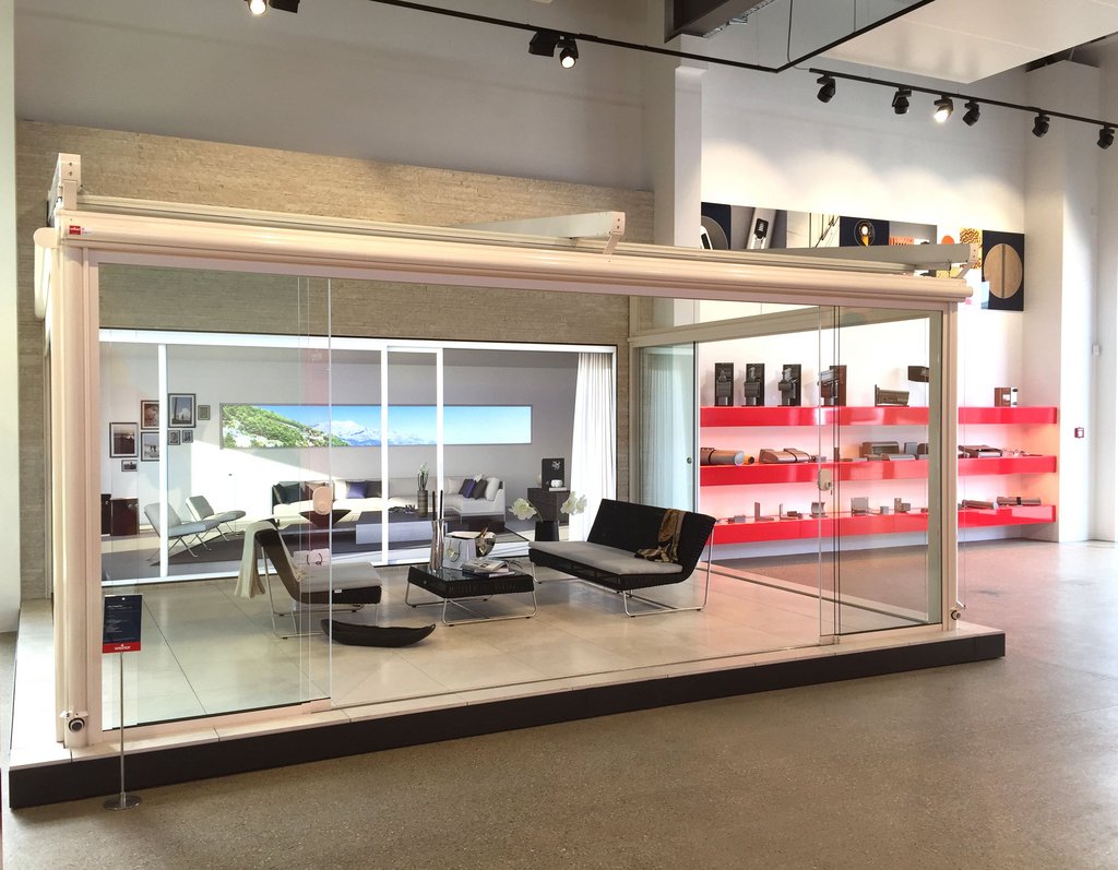 Showroom display featuring a glass structure with modern furnishings and a light aesthetic. Showroom display featuring a glass structure with modern furnishings and a light aesthetic.