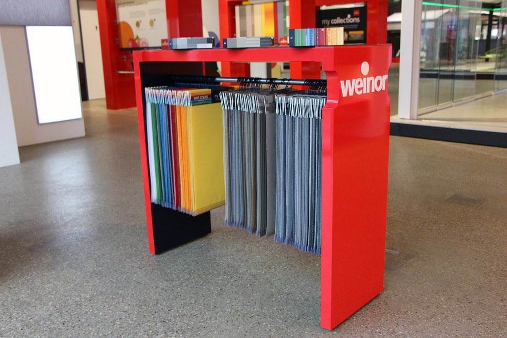 A red display stand holding various coloured samples, with grey, blue, yellow, and black hanging below. A red display stand holding various coloured samples, with grey, blue, yellow, and black hanging below.
